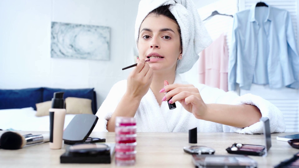 mujer que aplica lápiz labial con cepillo cosmético cerca de la mesa con cosméticos decorativos
 - Metraje, vídeo
