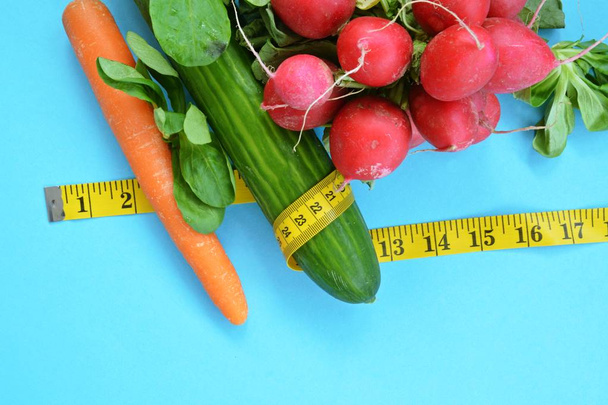 Verse knapperige groenten verpakt met een meetlint liggend op een einfabrigen base-concept voor gezond eten om gewicht te verliezen - Foto, afbeelding