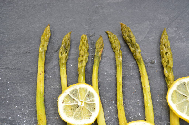 Свежеприготовленная зеленая спаржа с ломтиками лимона и посыпанная специями
   - Фото, изображение