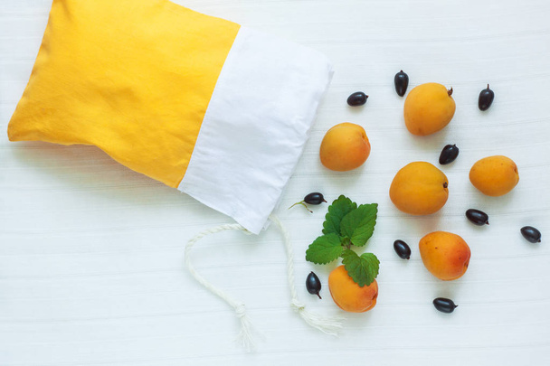 Top view of yellow cotton shopping bag with organic eco apricot fruits on white linen background. Zero waste. - Photo, Image