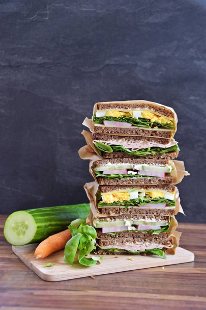 Various sandwiches of sunflower seed bread with cheese, sausage, egg and salad as a healthy diet are stacked on a dark background, next to a measuring tape as an allusion to fitness - Photo, Image