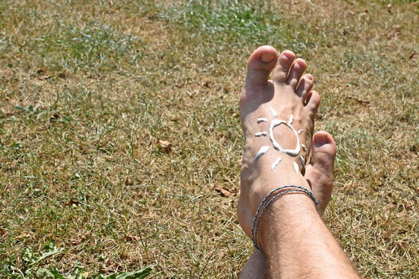 Konzept zum Schutz vor der Sonne an heißen Strandtagen mit einem männlichen Fuß mit Fußkettchen  - Foto, Bild