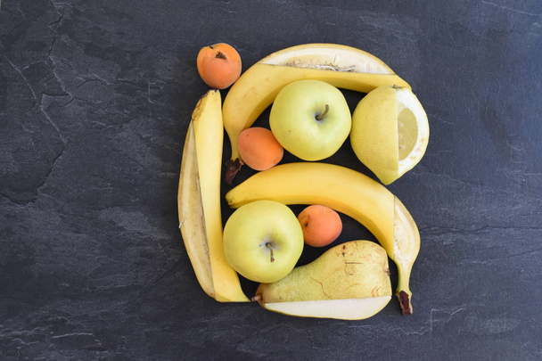 Een heleboel gele vruchten zoals appels, peren en bananen liggen op een plat oppervlak, met een mes een vierkant frame werd gesneden in de vrucht-perfect geregeld fruit als een frame - Foto, afbeelding