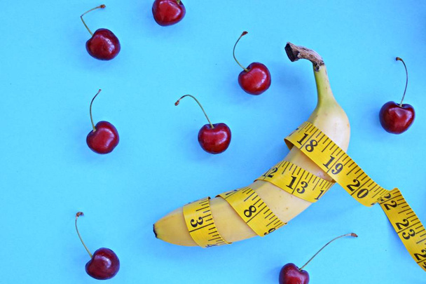 Different types of fruit, such as apples, cherries and bananas lie on a single-footed base and are wrapped in a measuring tape - concept for healthy weight loss that makes fun - 写真・画像