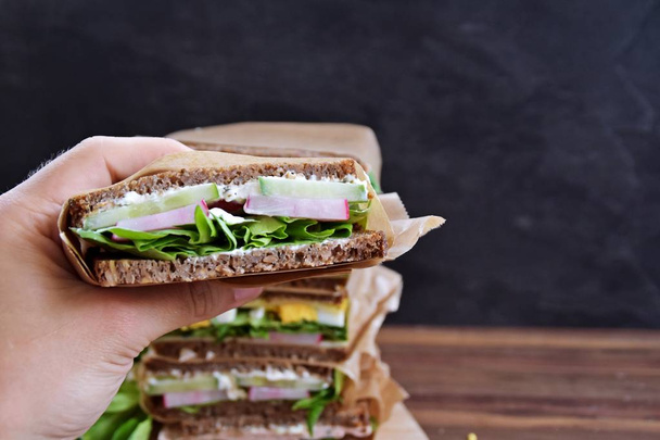 Verschiedene Sandwiches Sonnenblumenbrot mit Käse, Wurst, Ei und Salat als gesunde Ernährung stapeln sich auf dunklem Untergrund, neben einem Maßband als Anspielung auf Fitness  - Foto, Bild