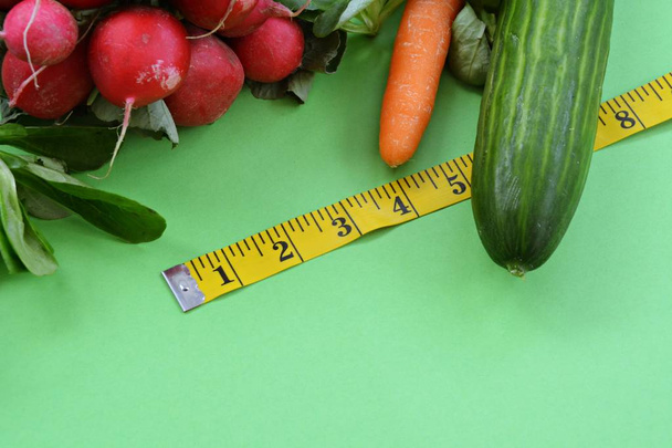 Frisches knuspriges Gemüse mit Maßband umwickelt auf einfabrigenem Boden liegend - Konzept für gesunde Ernährung zum Abnehmen - Foto, Bild