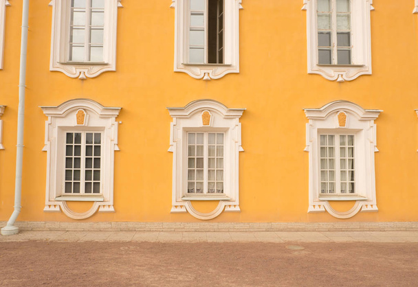 Window of an old building, palace. The frame is made of stucco in the Baroque style. White linen on a yellow background of the walls (ocher). Grand Peterhof Palace. Summer is a sunny day. - Fotoğraf, Görsel
