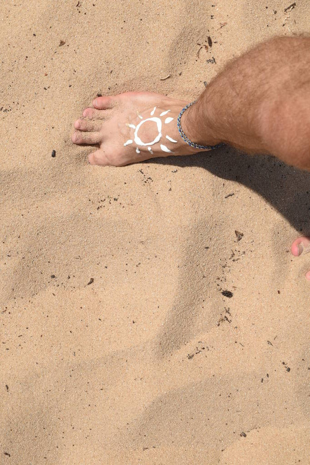 Έννοια για την προστασία από τον ήλιο σε ζεστές μέρες της παραλίας με ένα αρσενικό πόδι με ένα βραχιόλι  - Φωτογραφία, εικόνα