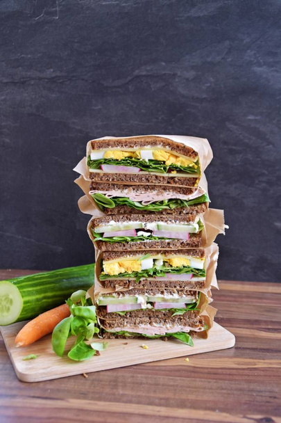 Várias sanduíches de pão de semente de girassol com queijo, salsicha, ovo e salada como uma dieta saudável são empilhadas em um fundo escuro, ao lado de uma fita métrica como uma alusão à aptidão
 - Foto, Imagem