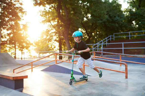 A boy on a scooter and in protective helmet do incredible stunts in skate park. Extreme jump. The concept of a healthy lifestyle and sports leisure - 写真・画像