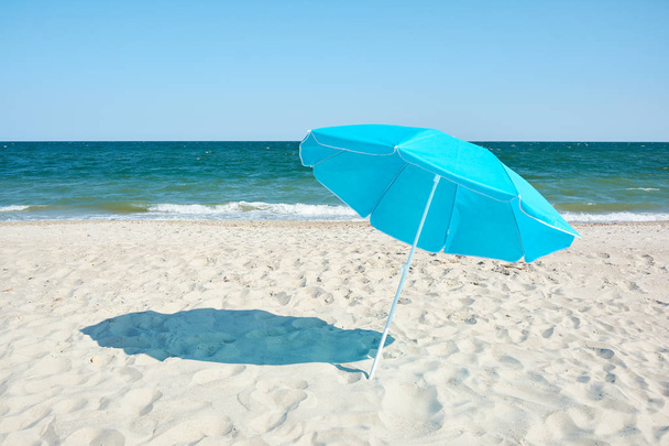 Бирюзовый пляжный зонтик на берегу моря. Солнечный жаркий день на песчаном пляже
. - Фото, изображение