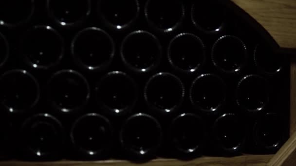Een close-up van de wijnflessen die in de kelder liggen. Glazen flessen rode wijn opgeslagen in houten rekken in een stenen kelder. Interieur ondergrondse wijnkelder in wijnmakerij - Video