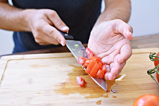 Een persoon snijdt een tomaat op een houten plank voor een verse knapperige gezonde salade-close-up op de handen van de persoon-concept voor gezonde voeding met verse biologische groenten  - Foto, afbeelding