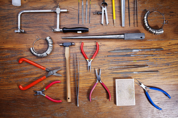 Top view of different goldsmiths tools on the jewelry workplace. Desktop for craft jewelry making with professional tools. Set of tools over rustic wooden background - 写真・画像