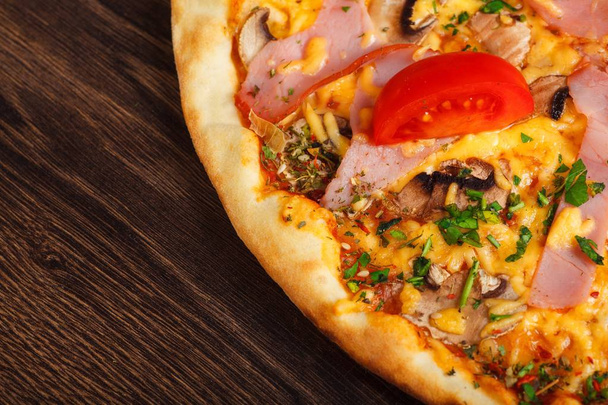 Zavřít horní pohled Italská Pizza s rozpuštěným sýrem mozzarella, rajčaty z červených třešní, šunkou a čerstvě zelenými bylinkami na hnědém stole ozdobený houbami, červenými papriky a třešňovýma rajčaty - Fotografie, Obrázek