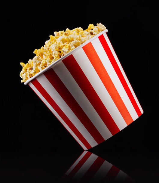 Paper striped bucket with popcorn isolated on black background - Foto, afbeelding