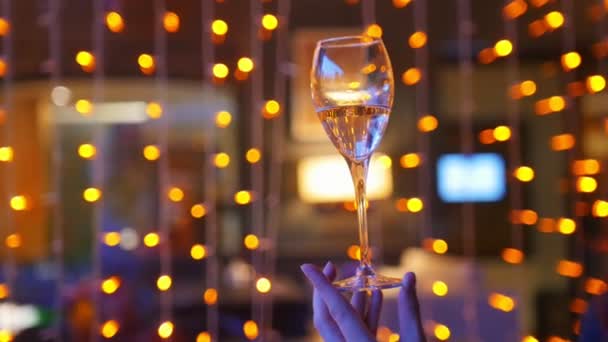 Ženská ruka držící sklenici šampaňského na pozadí oranžových světel - Záběry, video