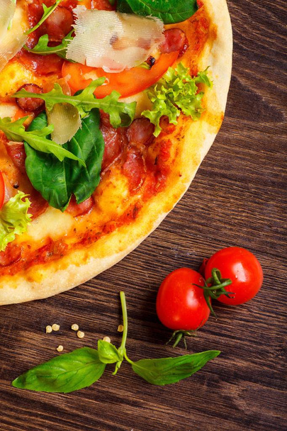 Lähikuva pizza Italian mozzarella, parmezan juustoa, punaisia tomaatteja ja tuoretta vihreää basilikaa, rucola ja kaali lehdet ruskea pöytä koristeltu mozzarella, paprika, kirsikka ja valssaustappi
 - Valokuva, kuva