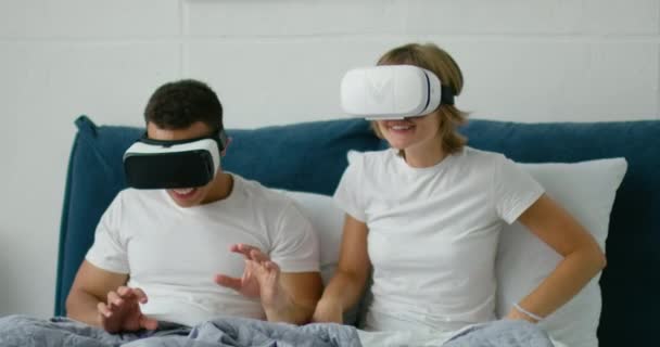Young couple lying in bed, watching 360 video in virtual reality headsets - Záběry, video