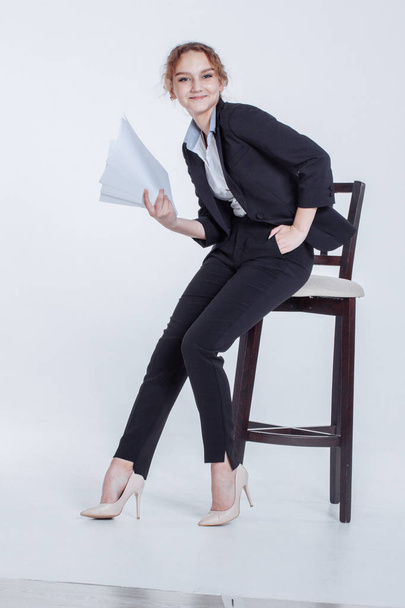 Young office worker girl in classic suit keeps clean sheets of paper isolated on white background. Cute financier lean on chair, holding clipboard in hands, thumbnail month's report in workplace. - Фото, изображение