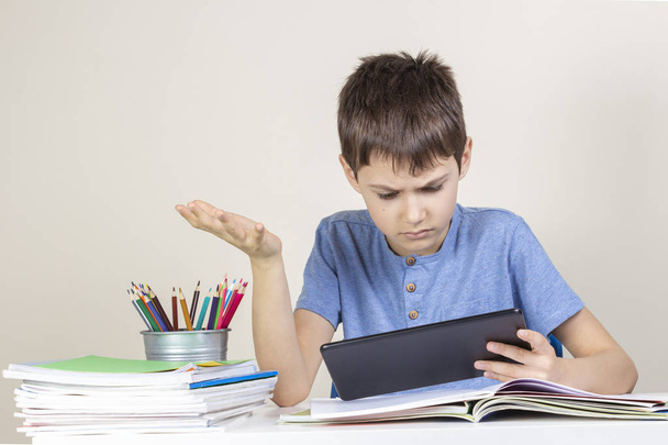 Hämmentynyt, yllättynyt lapsi, jolla on tabletti tietokone, joka istuu pöydässä kirjojen muistikirjoilla
 - Valokuva, kuva