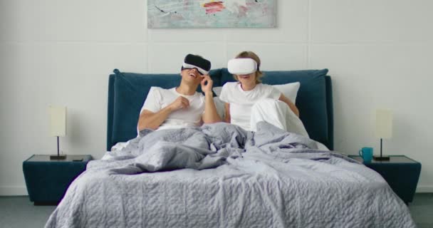 Pareja joven acostada en la cama, con los auriculares de realidad virtual puestos
 - Metraje, vídeo