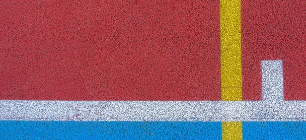 Fondo colorido de la cancha deportiva. Vista superior al suelo de goma de campo rojo y azul con líneas blancas y amarillas al aire libre
 - Foto, imagen