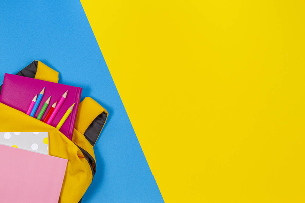 Back to school concept. Yellow backpack with school supplies on yellow and light blue background. Top view - Foto, afbeelding