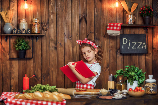 Pretty girl in checkered apron reading recipes book - Φωτογραφία, εικόνα
