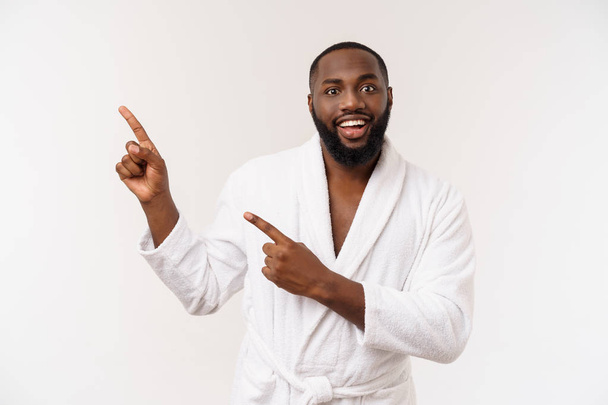 Zwarte kerel het dragen van een badjas wijzend vinger met verrassing en gelukkige emotie. Geïsoleerde over whtie achtergrond. - Foto, afbeelding