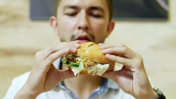 Ένας πεινασμένος άνθρωπος που τρώει ένα ζουμερό burger σε ένα φαστ φουντ εστιατόριο, νόστιμο φαγητό - Πλάνα, βίντεο