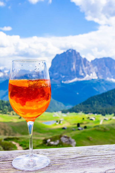 Uitzicht op de traditionele Italiaanse alcoholische drank Aperol Spritz op de achtergrond van kleurrijke Italiaanse weiden en de Dolomieten Alpen bergen. Village St. Cristina di Val Gardena Bolzano Seceda, Italië. - Foto, afbeelding