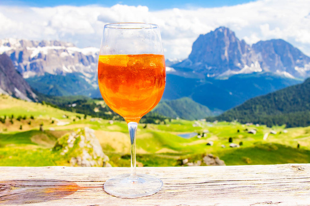 Widok na tradycyjny włoski napój alkoholowy Aperol Spritz na tle kolorowych włoskich łąk i gór Dolomitów Alp. wioska St. Cristina di Val Gardena Bolzano Seceda, Włochy. - Zdjęcie, obraz