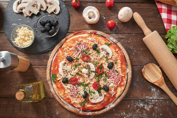 Homemade Pizza on wooden board, with tomatoes and salami, mushrooms, Italian style on old wooden table, top view - Foto, Imagem