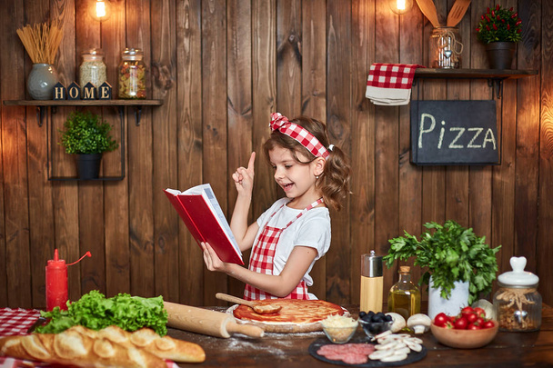 Pretty girl in checkered apron reading recipes book - Zdjęcie, obraz