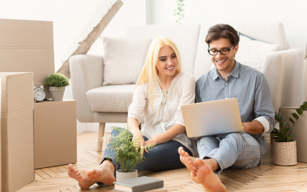 Cheerful couple sitting on floor using laptop in new house - Photo, Image