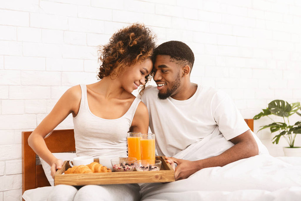 Feliz pareja negra disfrutando del desayuno en la cama
 - Foto, Imagen