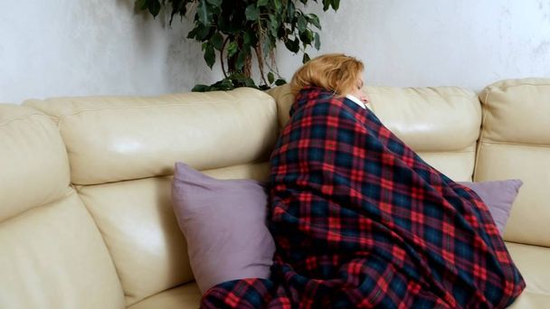woman in a house on the sofa lying under a plaid at home suffering from cold and fever. The concept of cold and flu virus - Photo, image
