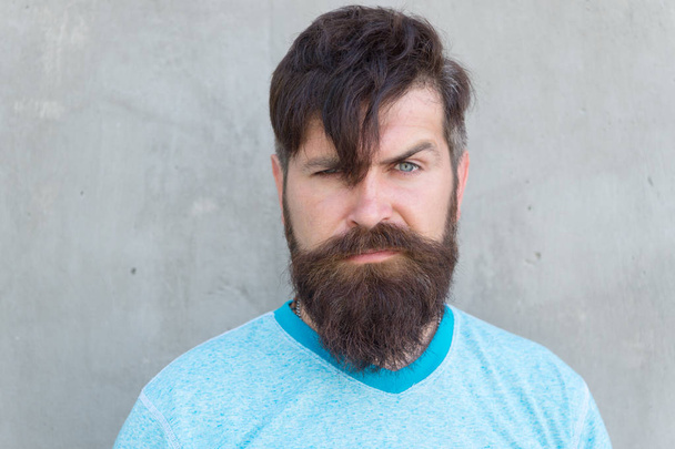 The bushy mustache is great. Bearded man with stylish mustache shape. Brutal hipster with textured mustache hair on unshaven face. Serious guy wearing long beard and mustache on grey wall - Photo, Image