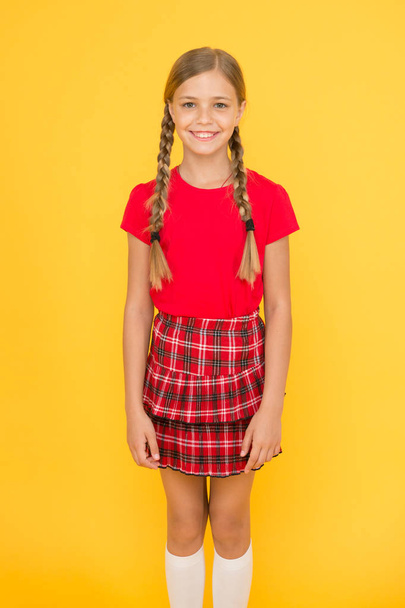 Adorable cutie. Cute little girl charming smile on yellow background. Happy small girl wearing red clothes. Girl with braided hair long braids. Adorable girl proud being pupil. Happy childhood - Фото, изображение