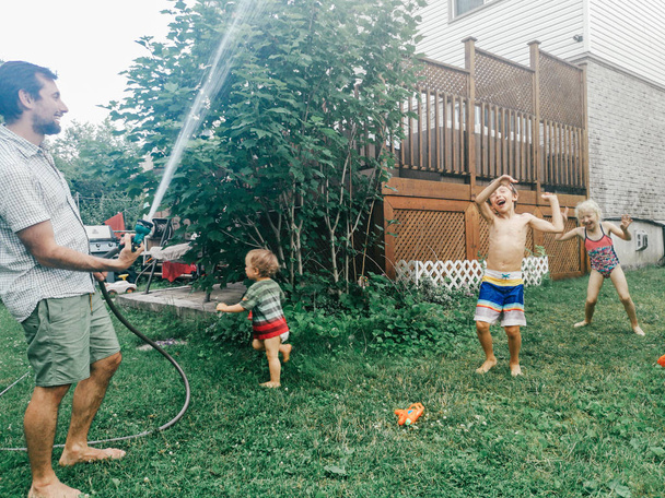Pai homem spray chuveiro de mangueira em crianças. Menino amigos menina irmãos espirrando jogando sob a água no quintal no dia quente de verão. Estilo de vida autêntico sincero momento familiar engraçado
. - Foto, Imagem