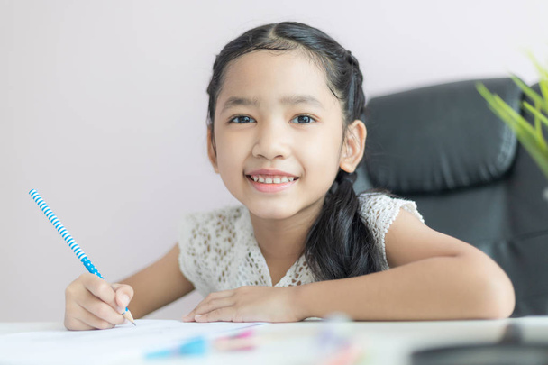 Piccola ragazza asiatica utilizzando la matita per scrivere sulla carta facendo h
 - Foto, immagini