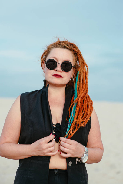 crazy funny grunge punk redhead woman with dreadlocks in office clothes and sunglasses in the desert  - Photo, Image