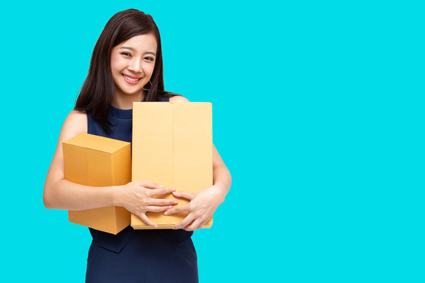 Joven empresario asiático sosteniendo paquete aislado sobre fondo azul, propietario de negocio adolescente en línea preparándose para la entrega del envío
 - Foto, Imagen