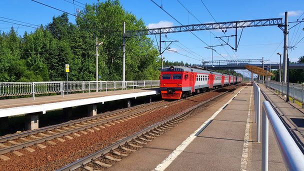 赤い郊外の列車は晴れた日に夏に駅に到着します。途中で列車を持つ鉄道プラットフォーム. - 写真・画像