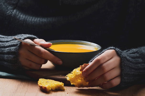 Female hand holding a  bowl with pumpkin cream soup. Cozy comfort concept. - Foto, immagini