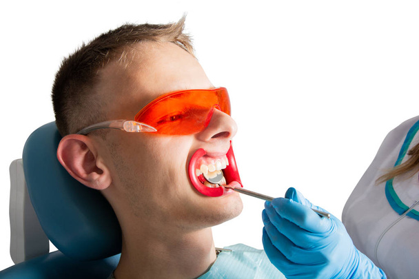 Odontología. Examen de los dientes con la ayuda de un primer plano de espejo dental. Joven paciente en la silla dental sobre fondo blanco aislado
. - Foto, Imagen
