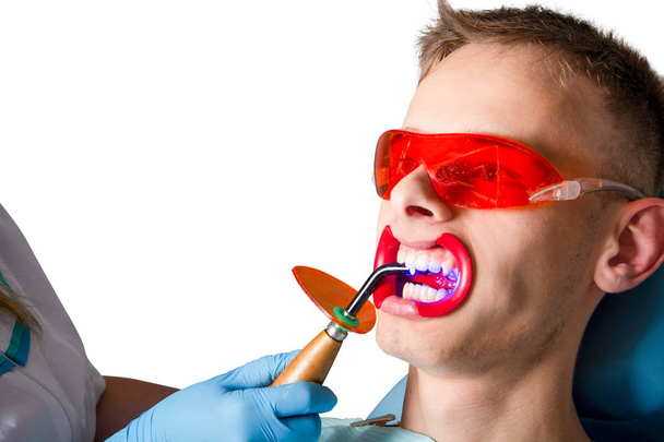 歯学。紫外線ランプクローズアップで充填物の重合。患者は孤立した白い背景の歯科椅子の男性である. - 写真・画像