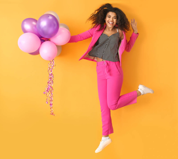 Portrait of jumping African-American woman with air balloons on color background - Foto, afbeelding
