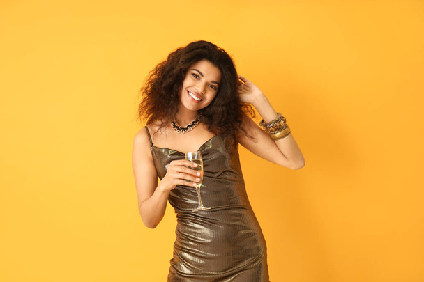 Portrait of happy African-American woman with glass of champagne on color background - Photo, Image